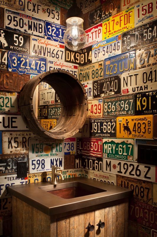 a sink in a room with lots of license plates on the wall and a round mirror above it