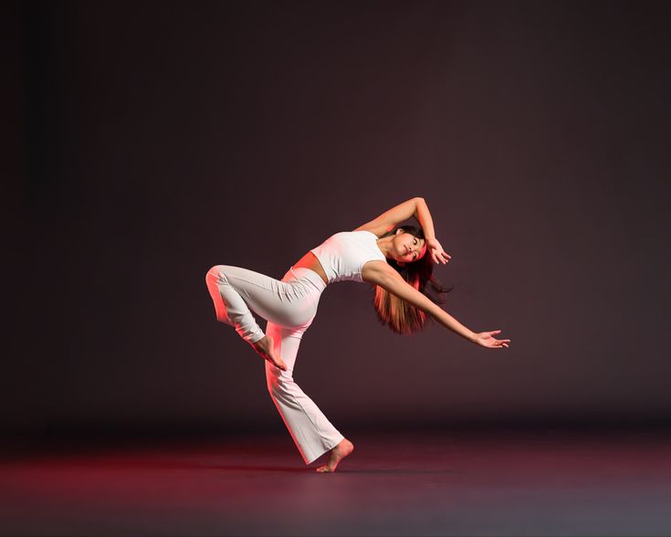 a woman in white is doing a dance move on a red and black background with her arms stretched out