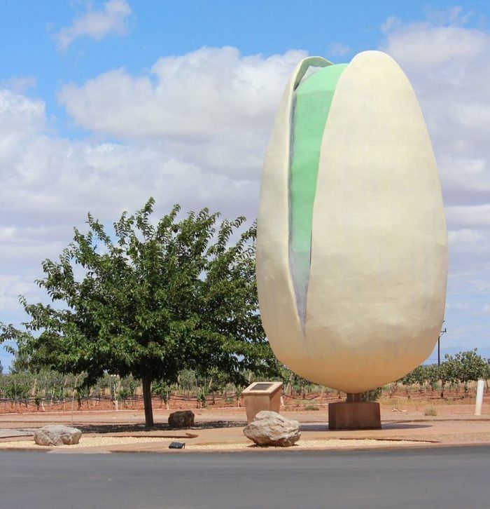 a large white sculpture sitting on the side of a road next to a green tree