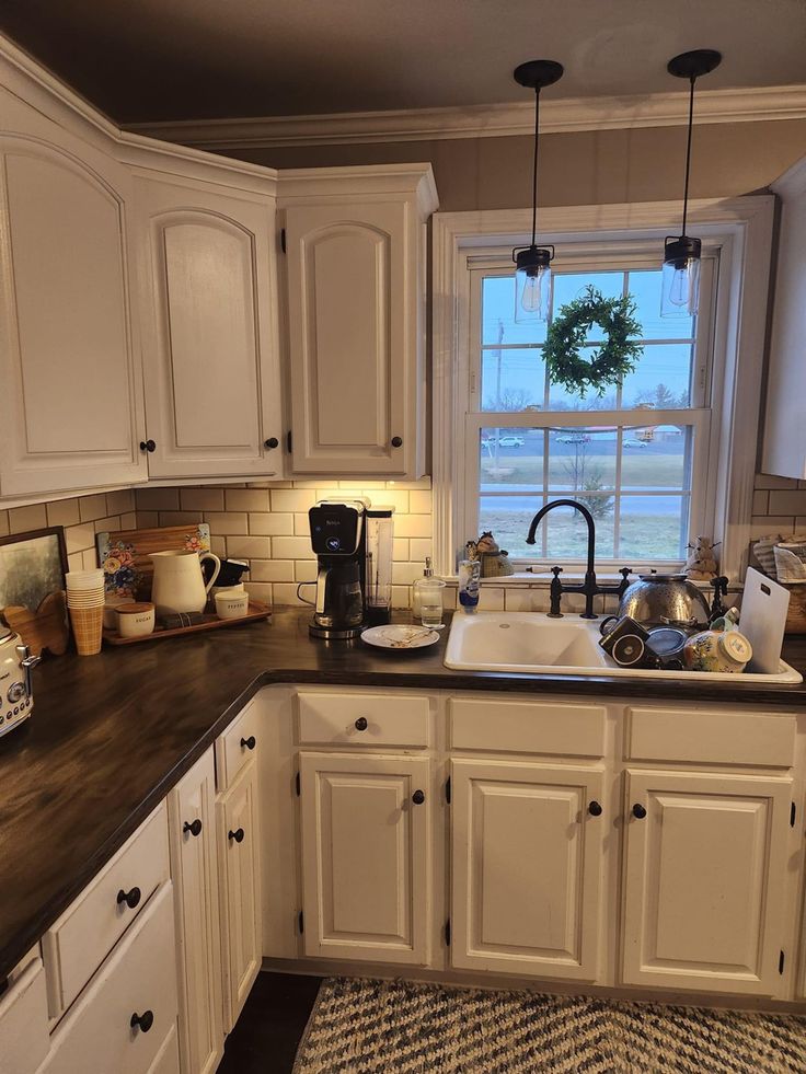 a kitchen with white cabinets and black counter tops is pictured in this image, there are pots on the window sill