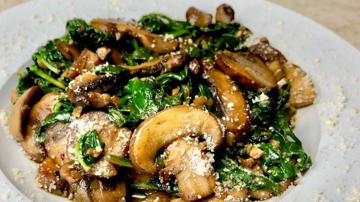 a white plate topped with mushrooms, spinach and parmesan sprinkled cheese