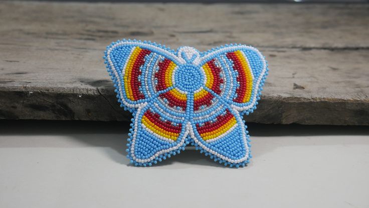 a beaded butterfly sitting on top of a piece of wood