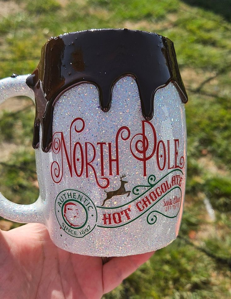 a hand holding a frosted coffee mug with the words north pole hot chocolate on it