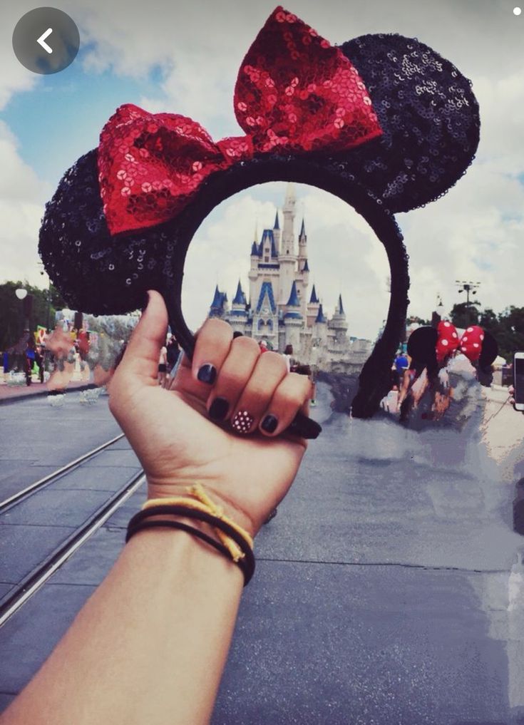 a person holding up a minnie mouse ears in front of a castle