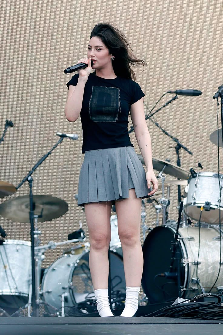 a woman standing on top of a stage with a microphone in her hand and wearing a skirt