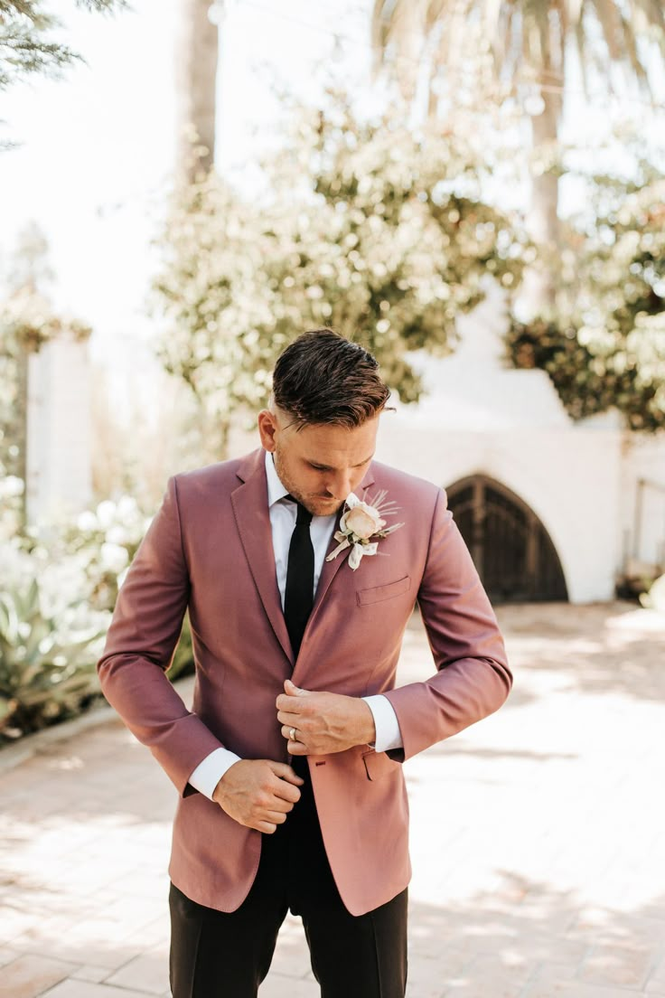 a man in a pink suit and black tie is looking down at his pocket square