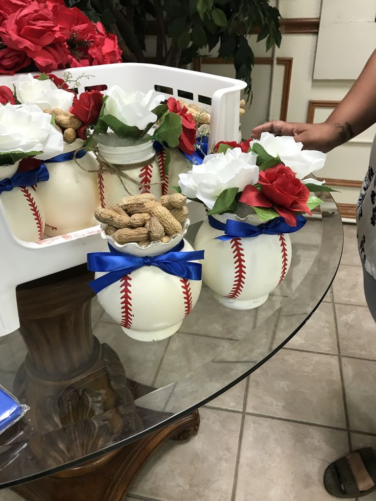 a table topped with vases filled with flowers and baseball balls sitting on top of a glass table