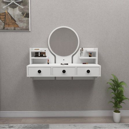 a white vanity with two drawers and a round mirror on the wall next to a potted plant