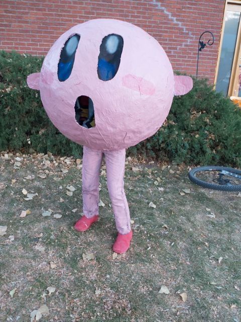 a person in a pink costume standing next to a brick building with large eyes and mouth