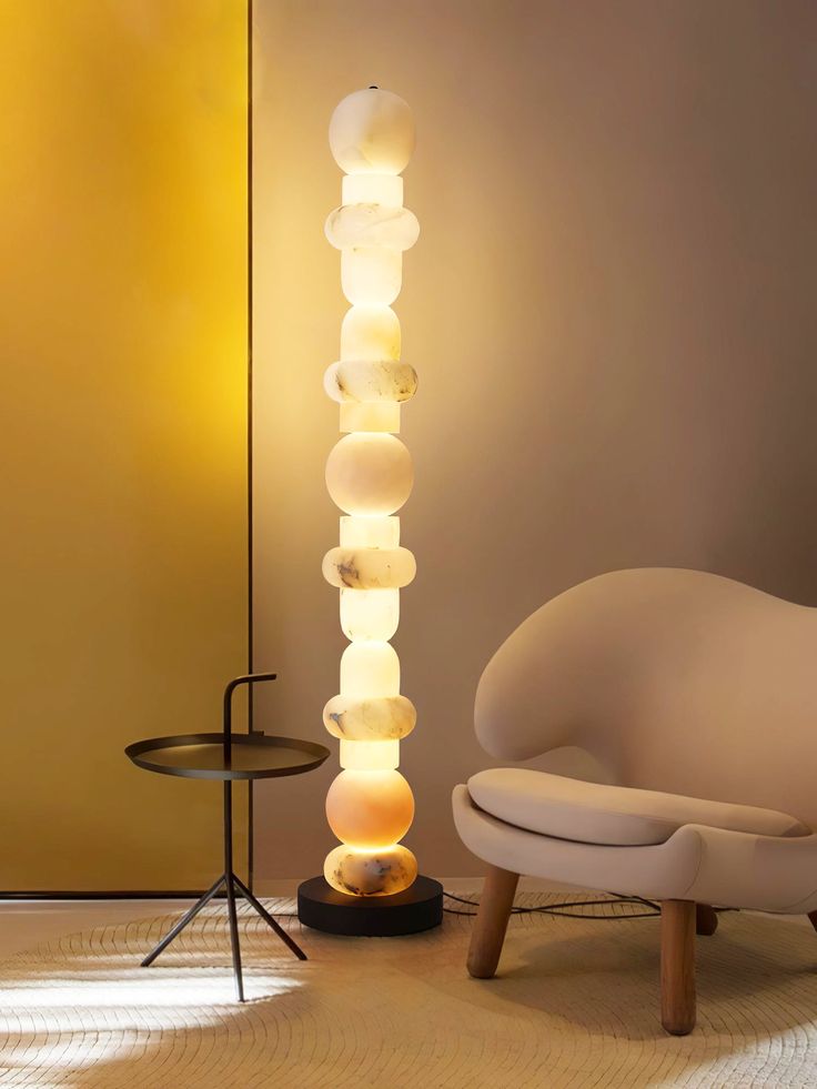 a white chair sitting next to a tall lamp on top of a wooden table in front of a yellow wall