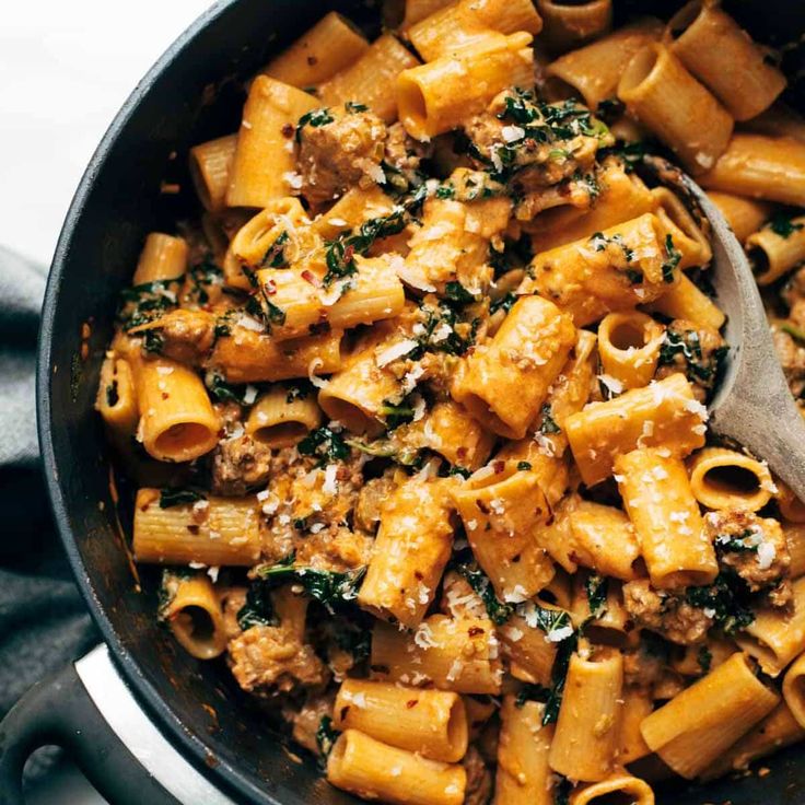 a skillet filled with pasta and sauce on top of a marble counter next to a wooden spoon