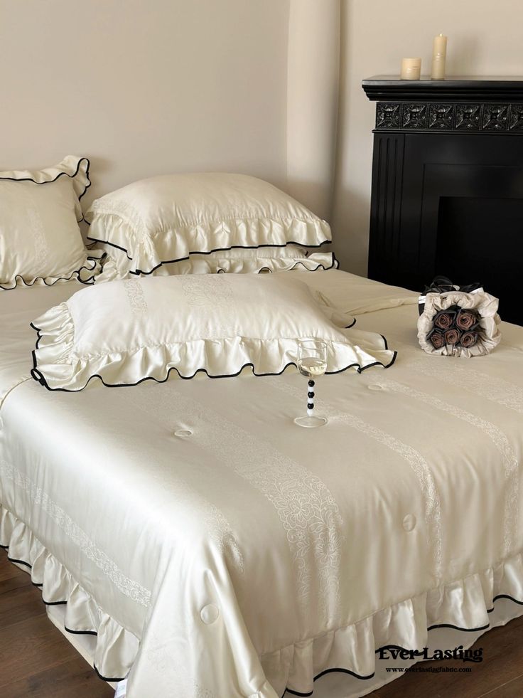 a bed with white sheets and pillows on it next to a black fireplace mantel