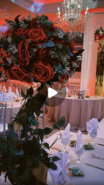 an arrangement of flowers and greenery on a table in a banquet hall with chandelier