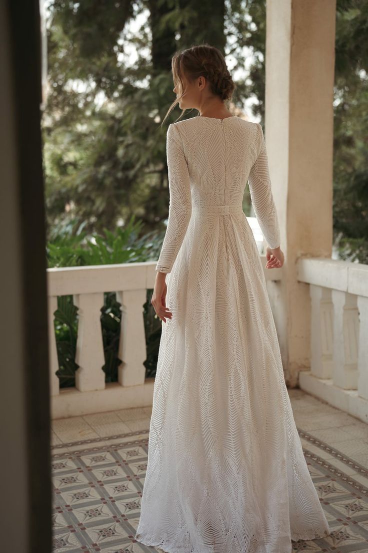 a woman in a long white dress standing on a porch with her back to the camera