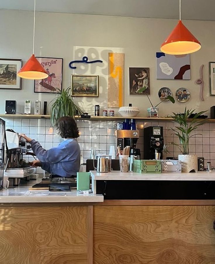 a woman sitting at a counter in front of a coffee machine and some pictures on the wall