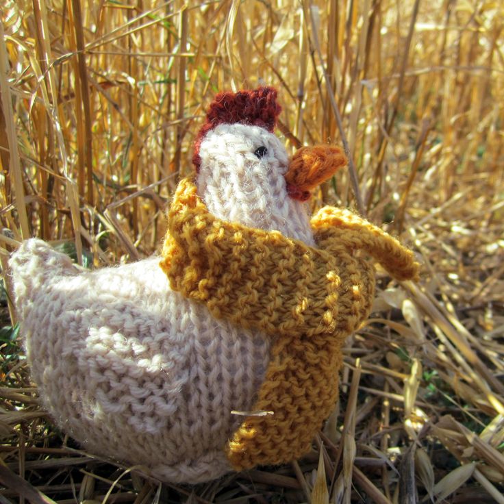 a knitted chicken wearing a scarf in the middle of some dry grass and straw