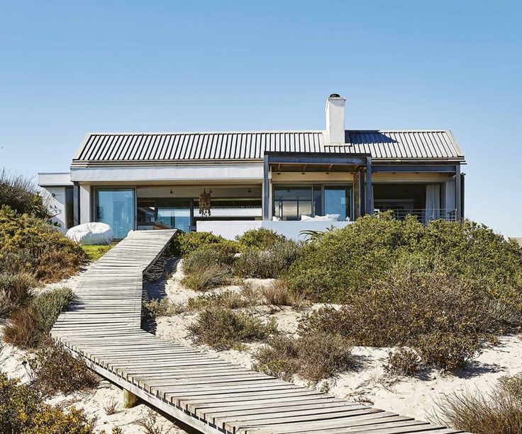 a house on the beach with a wooden walkway leading to it's front door