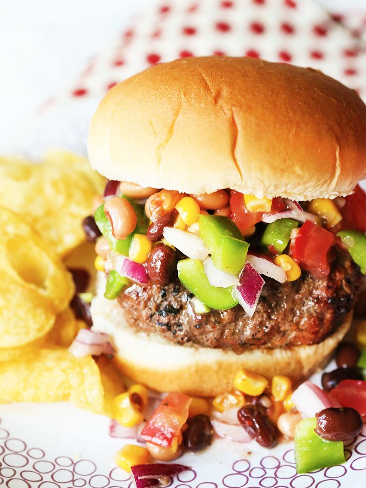 a hamburger with lettuce, tomato, and other toppings next to chips