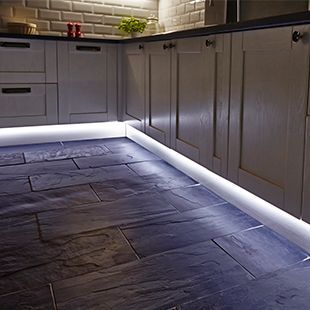 a kitchen with white cabinets and black slate flooring is lit up by leds