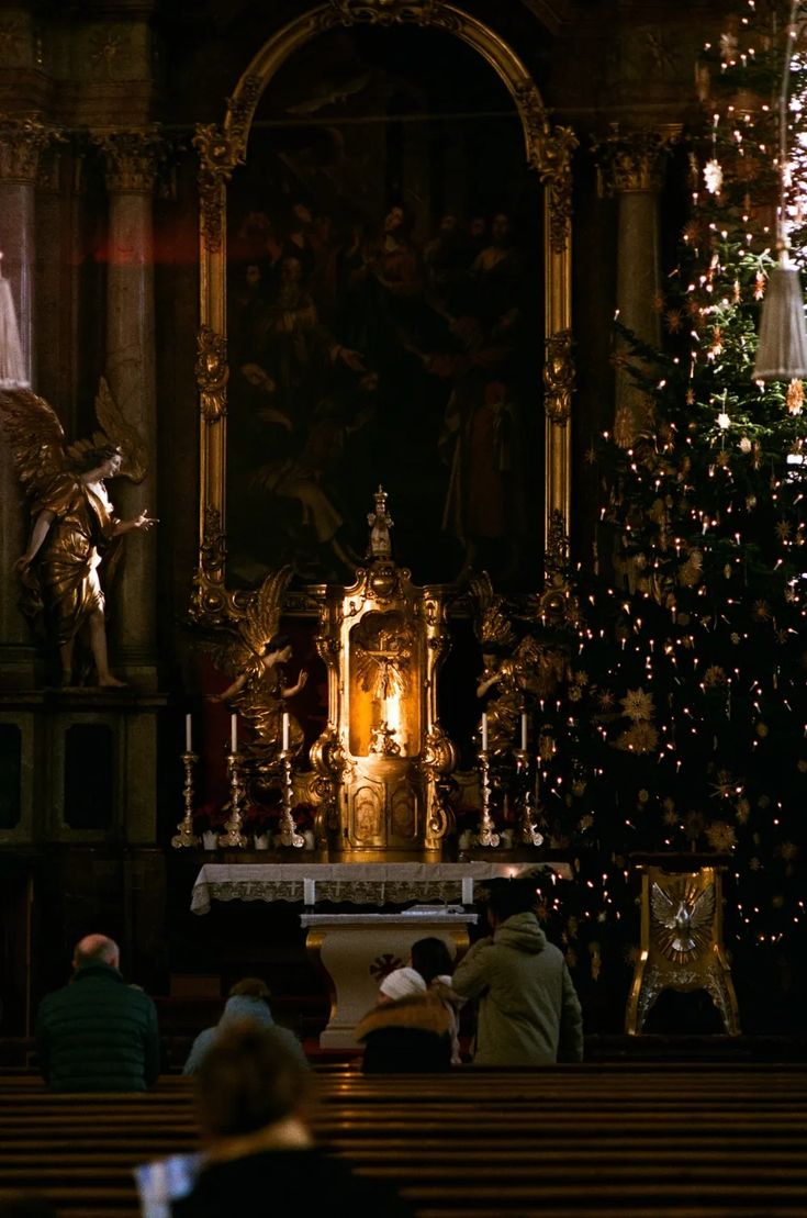 people are sitting at the alter in front of a christmas tree with lights on it