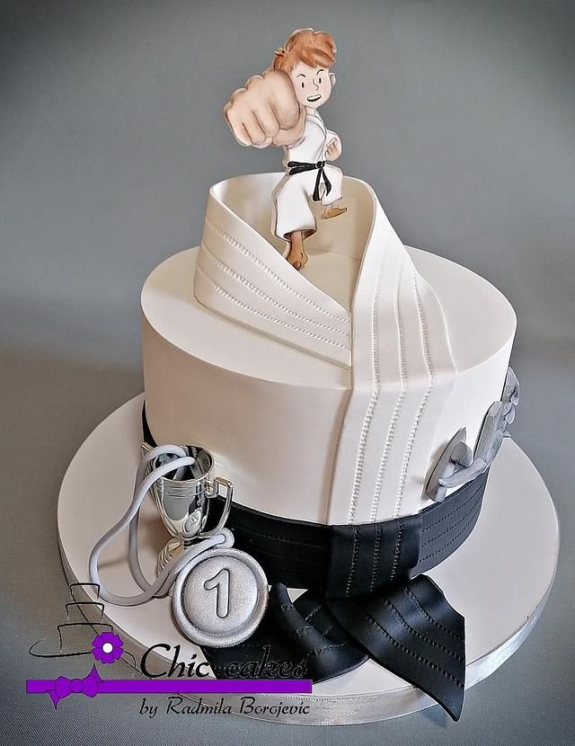 a white cake with a karate figure on top and black ribbon around the edge, sitting on a silver platter