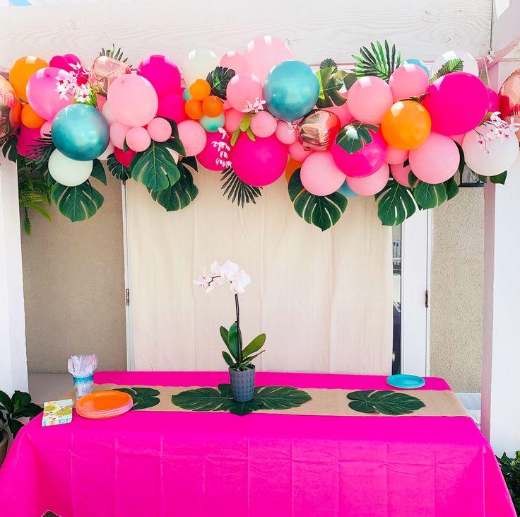 a pink table topped with balloons and flowers