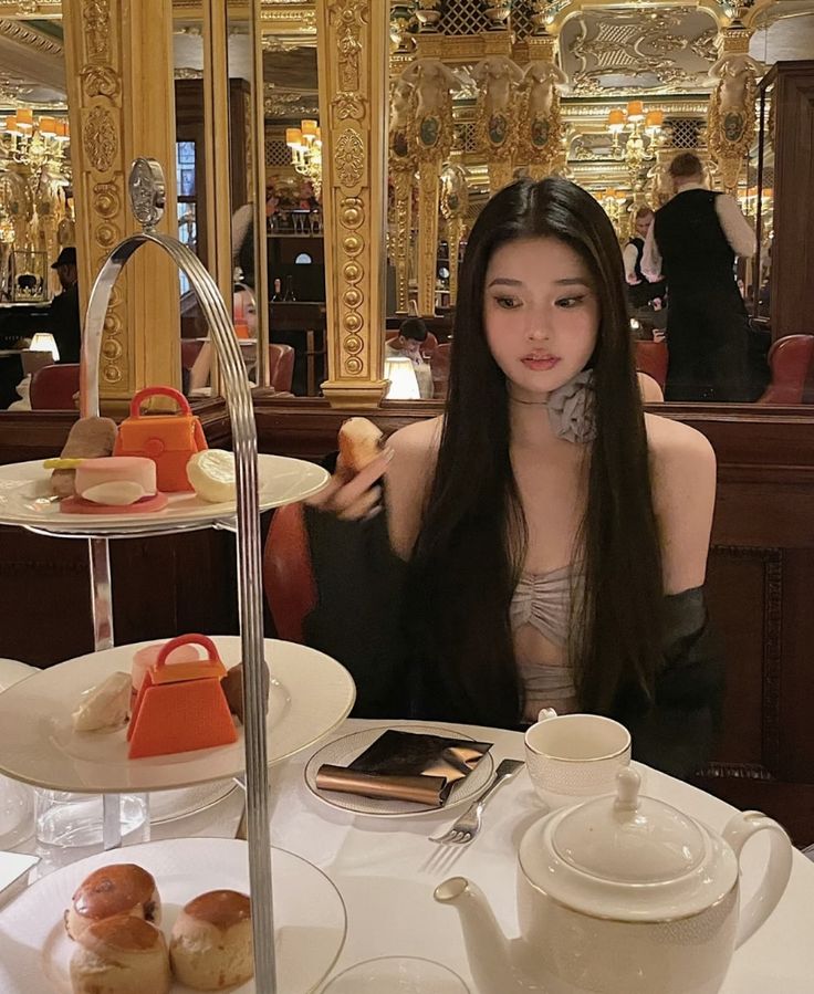 a woman sitting at a table with plates and cups on it, in a fancy restaurant