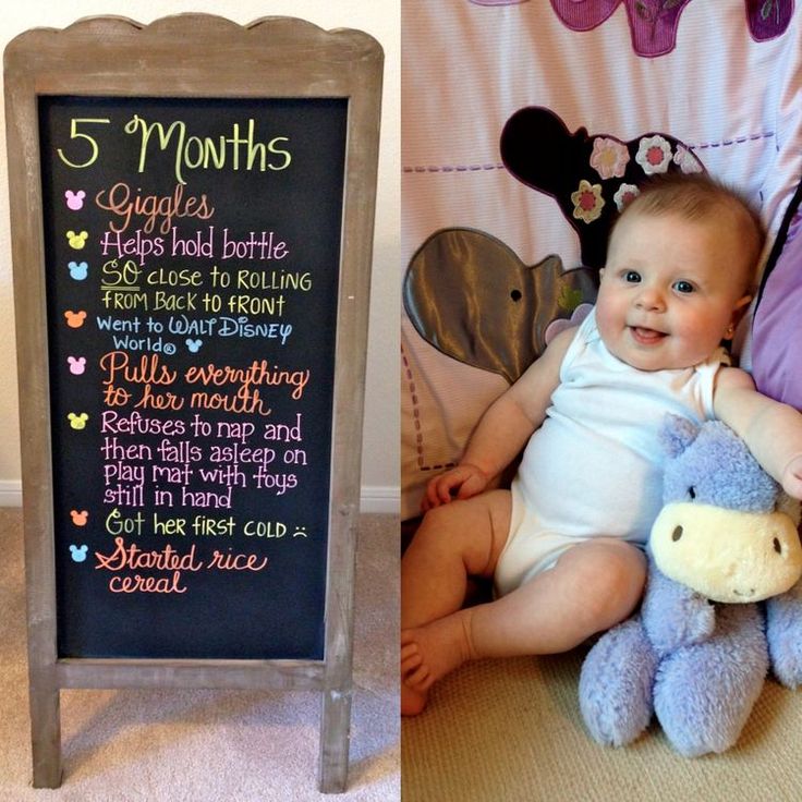 a baby sitting next to a chalkboard sign and stuffed animal