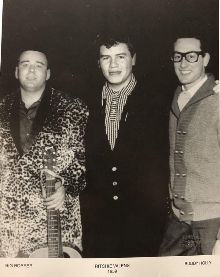 three men standing next to each other in front of a black and white photo with one holding a guitar