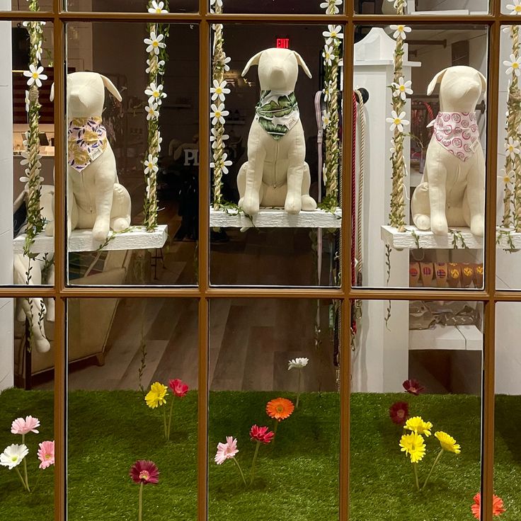 two white dogs sitting in front of a window with fake flowers on the windowsill