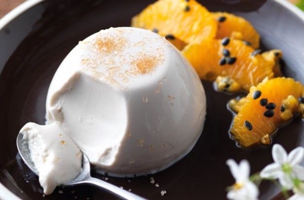 a plate topped with oranges and ice cream on top of a wooden table next to flowers