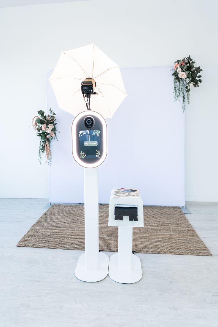 there is an electronic device on display in front of a white wall and flower arrangements