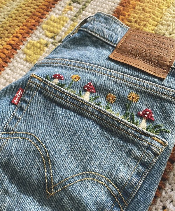 a pair of jeans with embroidered flowers on them sitting on a colorful rug next to a stuffed animal