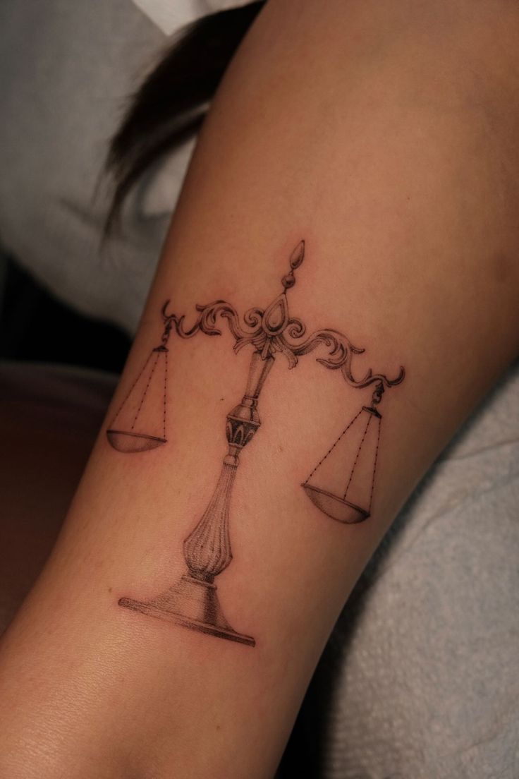 a woman's arm with a tattoo on it that has an image of a balance scale