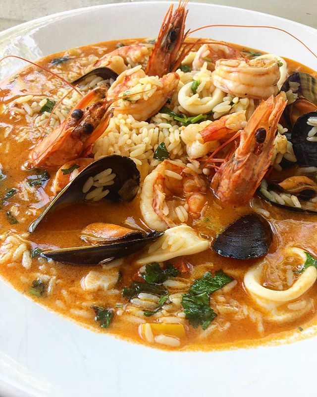 a white plate topped with pasta and shrimp next to mussels on top of rice