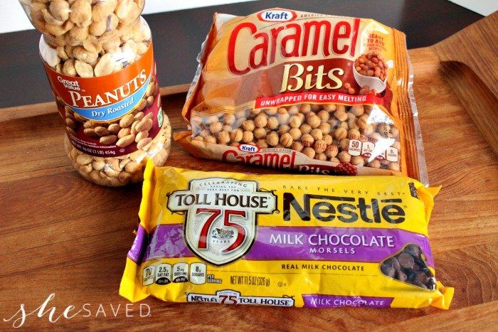 some nuts and other snacks are sitting on a wooden tray next to a jar of peanut butter