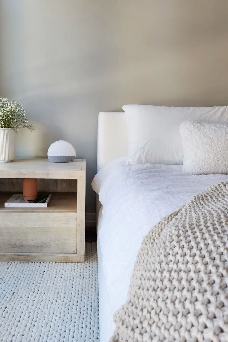 a white bed sitting next to a nightstand with a vase filled with flowers on top of it