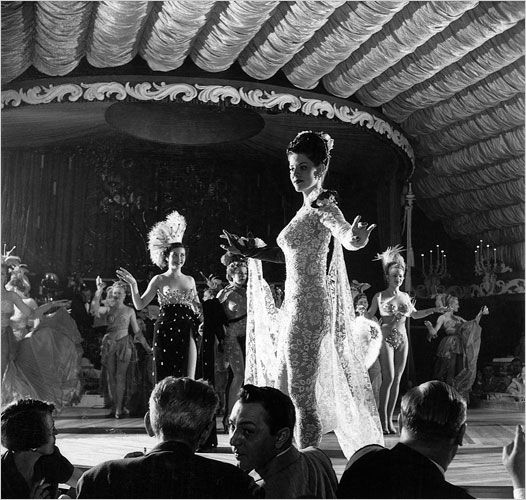 a black and white photo of some women in dresses on stage with other people around