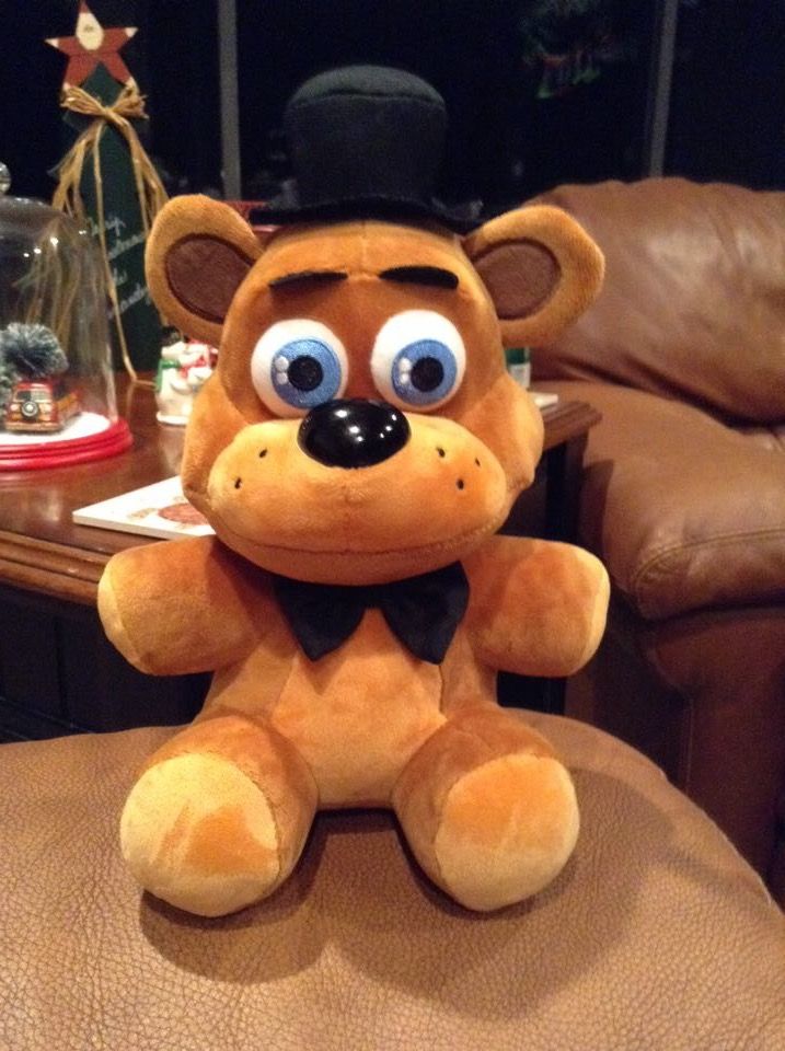 a stuffed animal with big eyes and a hat on top of a leather chair in a living room