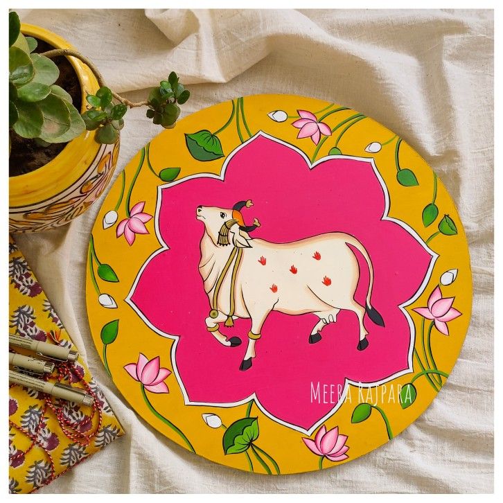 a yellow and pink plate with a cow painted on it next to a potted plant