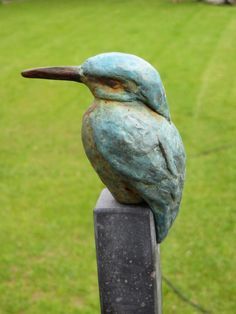 a statue of a bird sitting on top of a wooden post in front of a grassy field