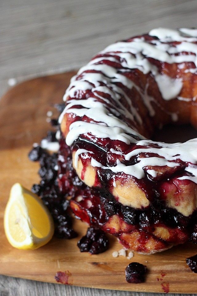 a blueberry bundt cake with icing on a cutting board next to a lemon wedge