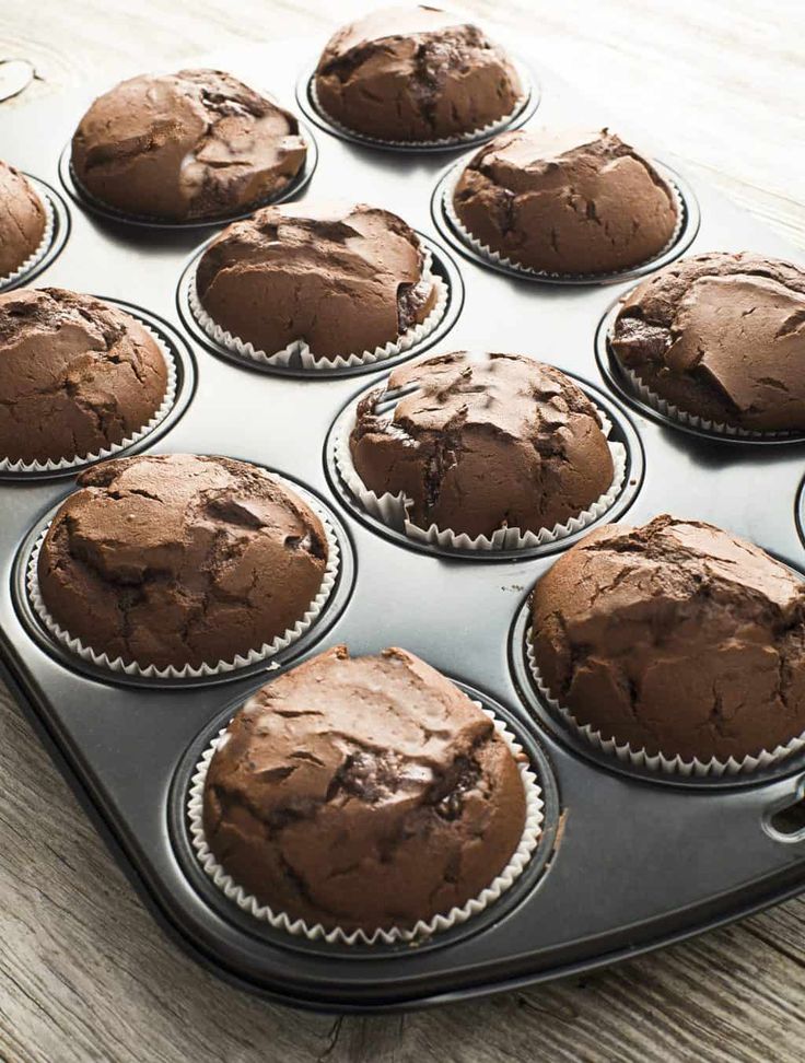 a muffin tin filled with chocolate cupcakes on top of a wooden table