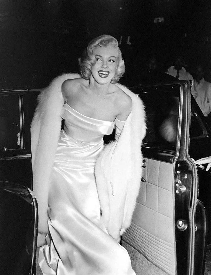 marilyn monroe in an evening gown and fur stoler leaning out the door of a car