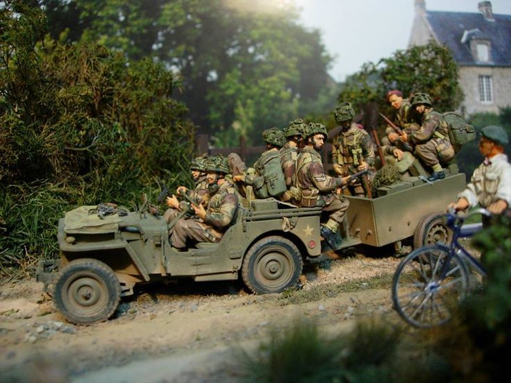 a group of men riding on the back of an army truck next to a forest