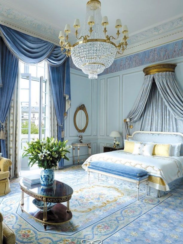 a bedroom with blue and white walls, chandelier, couches, chairs and paintings on the wall