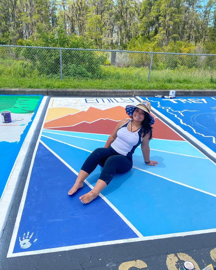 a woman sitting on the ground in front of a basketball court with painted lines and numbers