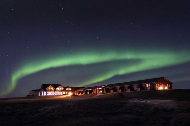 the aurora lights shine brightly in the night sky over a large house on a hill