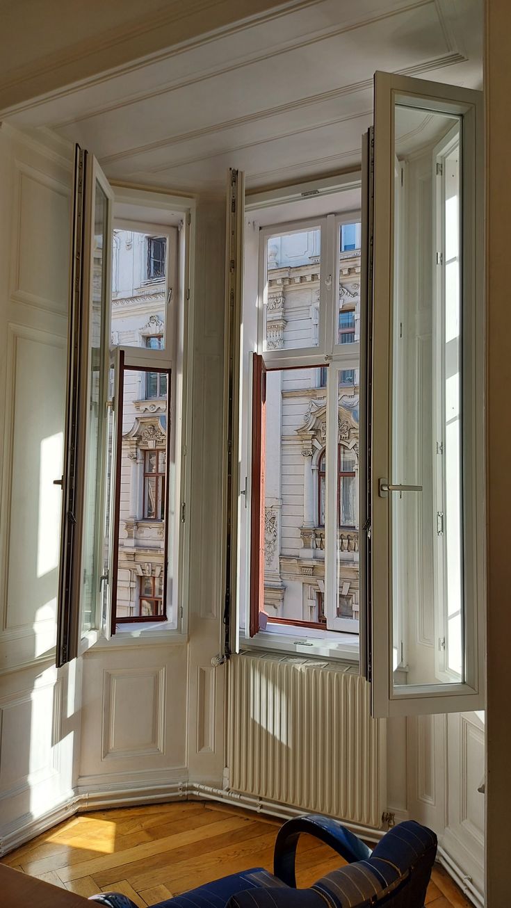 an empty room with two large windows and wooden floors