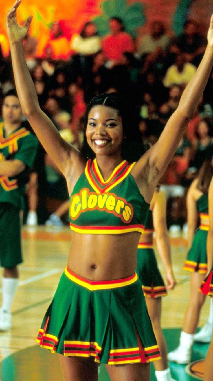 a woman in a green and yellow cheerleader uniform on a basketball court with her arms up